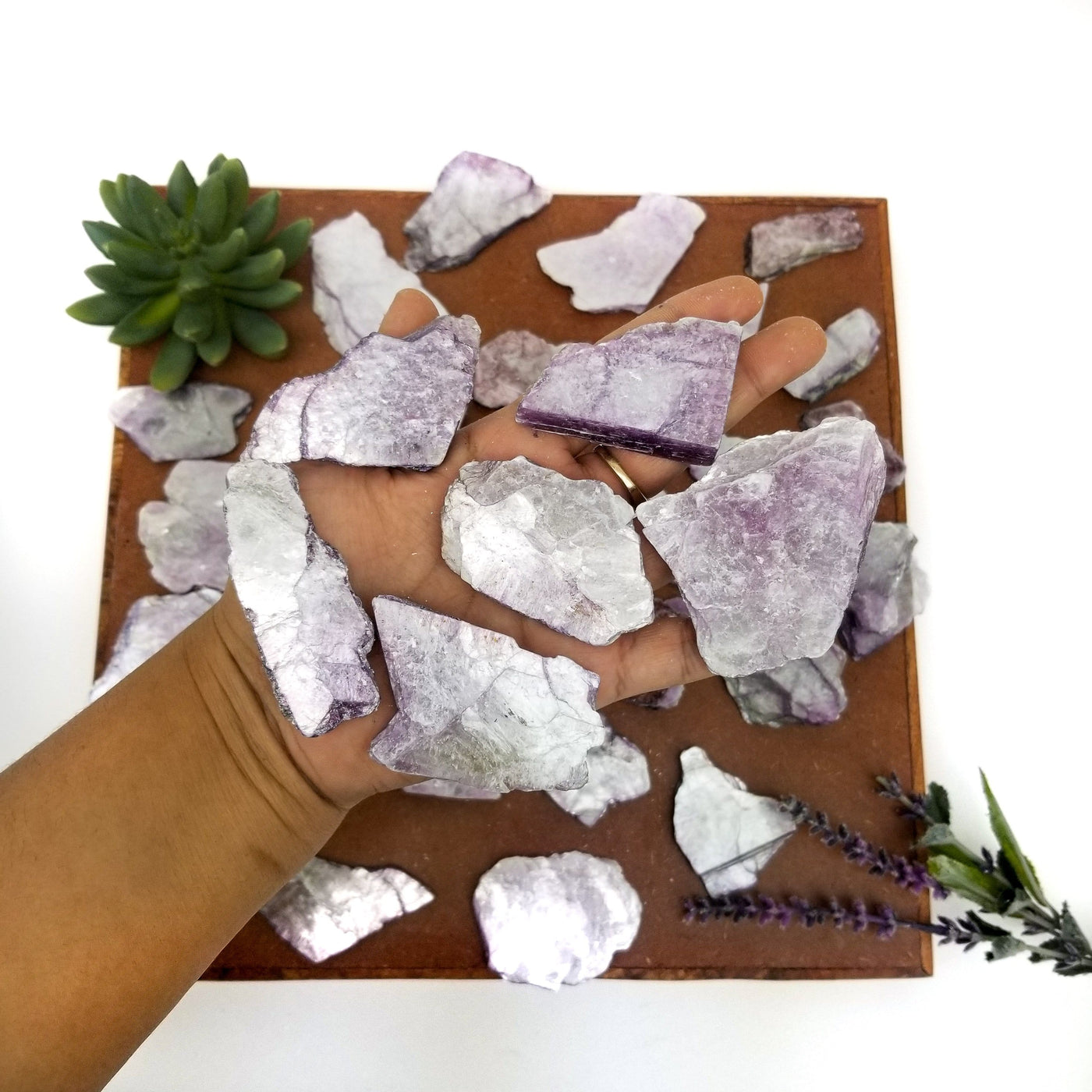 hand holding up 5 lepidolite slices with others blurred in the background on brown platter