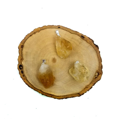3 citrine pendants with silver bails on wooden coaster