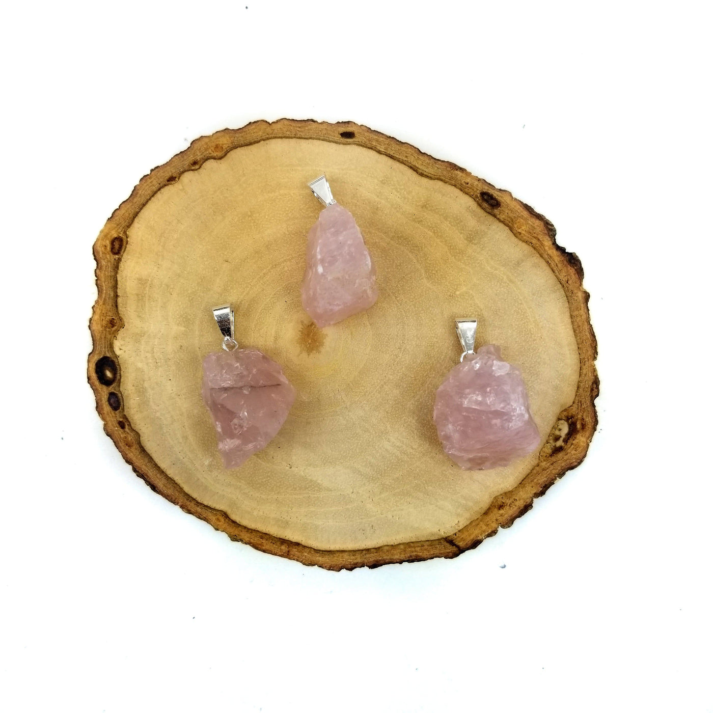 3 rose quartz pendants with silver bails on wooden coaster