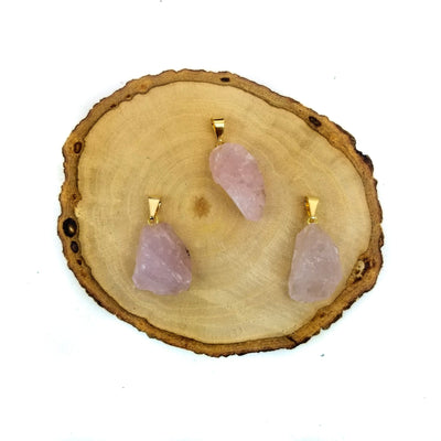 3 rose quartz pendants with gold bails on wooden coaster