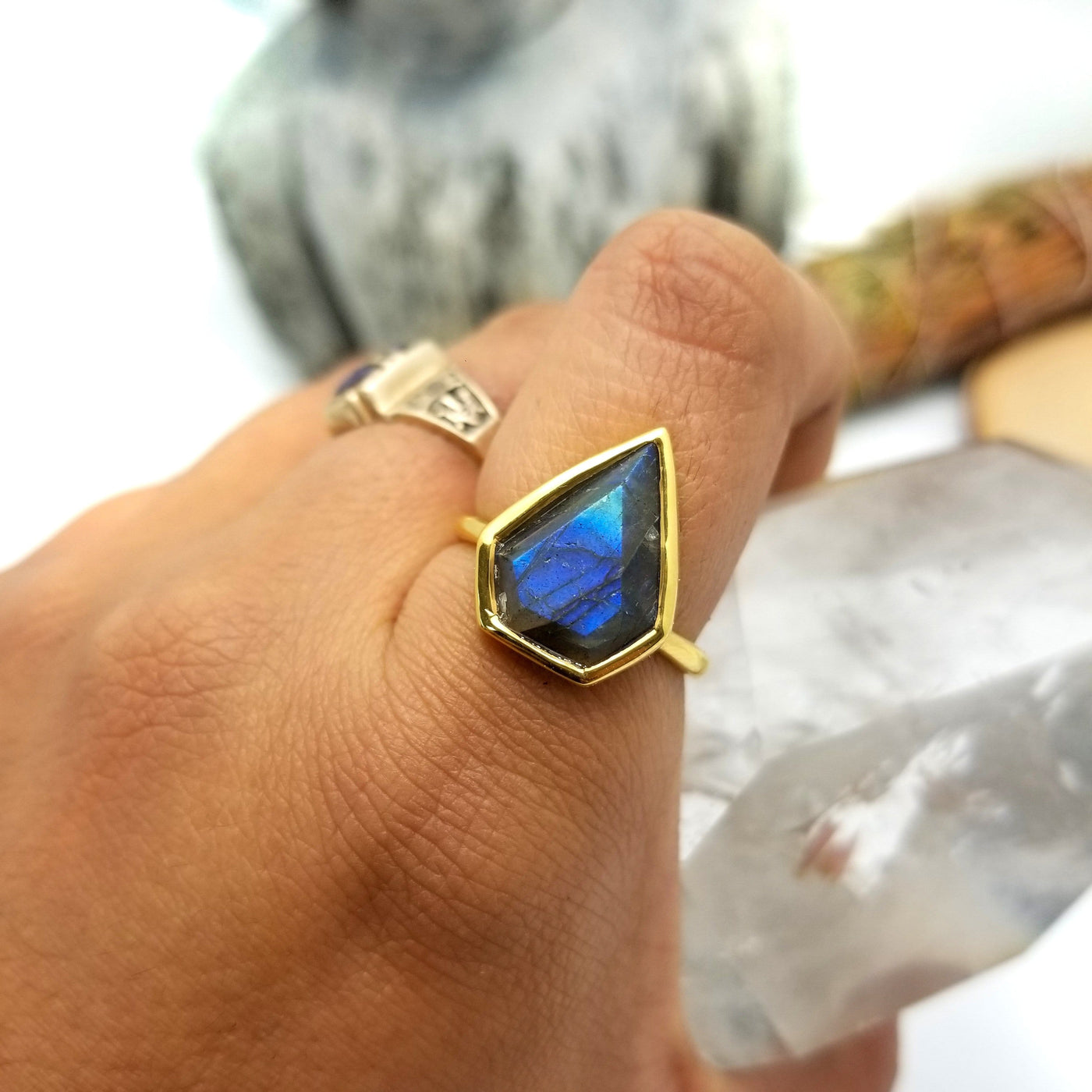 finger wearing labradorite arrowhead ring in gold with decorations in the background