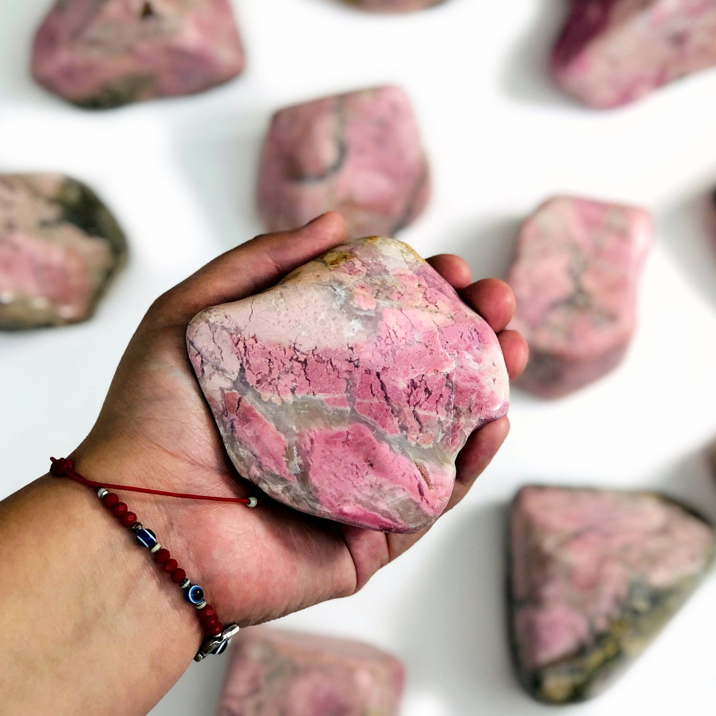 Hand holding up Rhodonite Tumbled Polished Stone with others scattered in the background