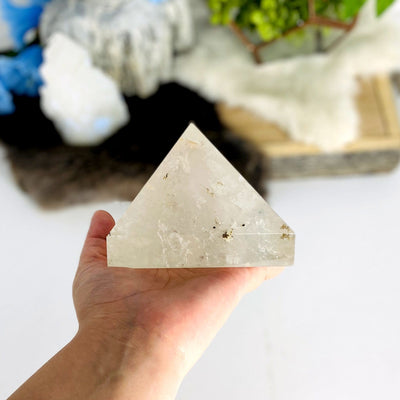 handholding up Crystal Quartz Pyramid with decorations in the background