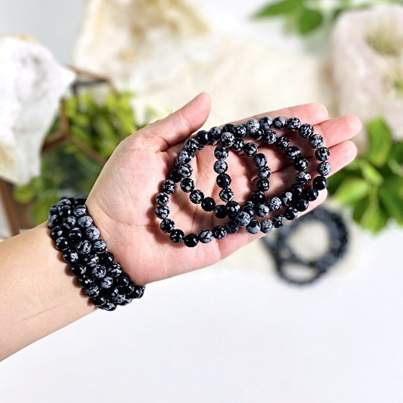 three snowflake obsidian round bead bracelets in hand and three more on wrist for size reference and possible variations