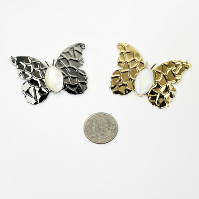gold and gunmetal butterfly pendants with a mother of pearl center next to quarter for size reference 