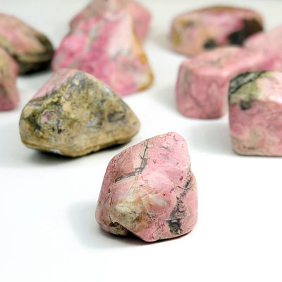 Rhodonite Tumbled Polished Stone up close with others blurred on white background