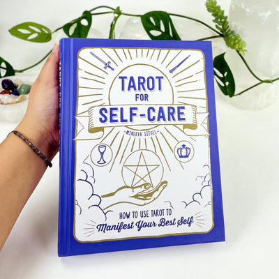 A book held by a hand , The title is Tarot for Self-Care by Minerva Siegel