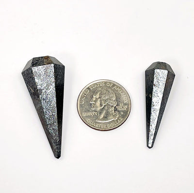 two different sized hematite pendulum points places next to a quarter for size reference