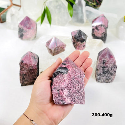 Hand holding 300-400g Rhodonite Point with others blurred in the background with decorations