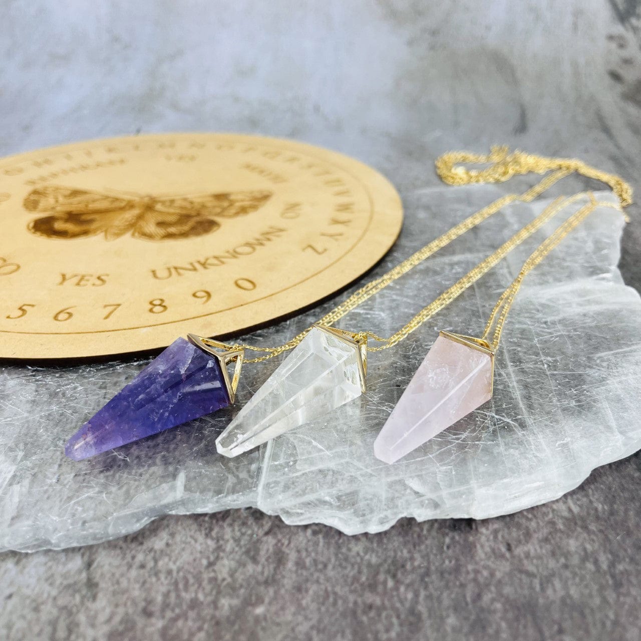 Rose Quartz Amethyst and Crystal Quartz Pendulum Necklaces laying on a table