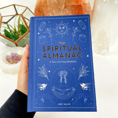 hand holding up Your Spiritual Almanac by Joey Hulin with decorations in the background