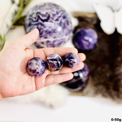 Chevron Amethyst Polished Spheres in a hand, size under 50g