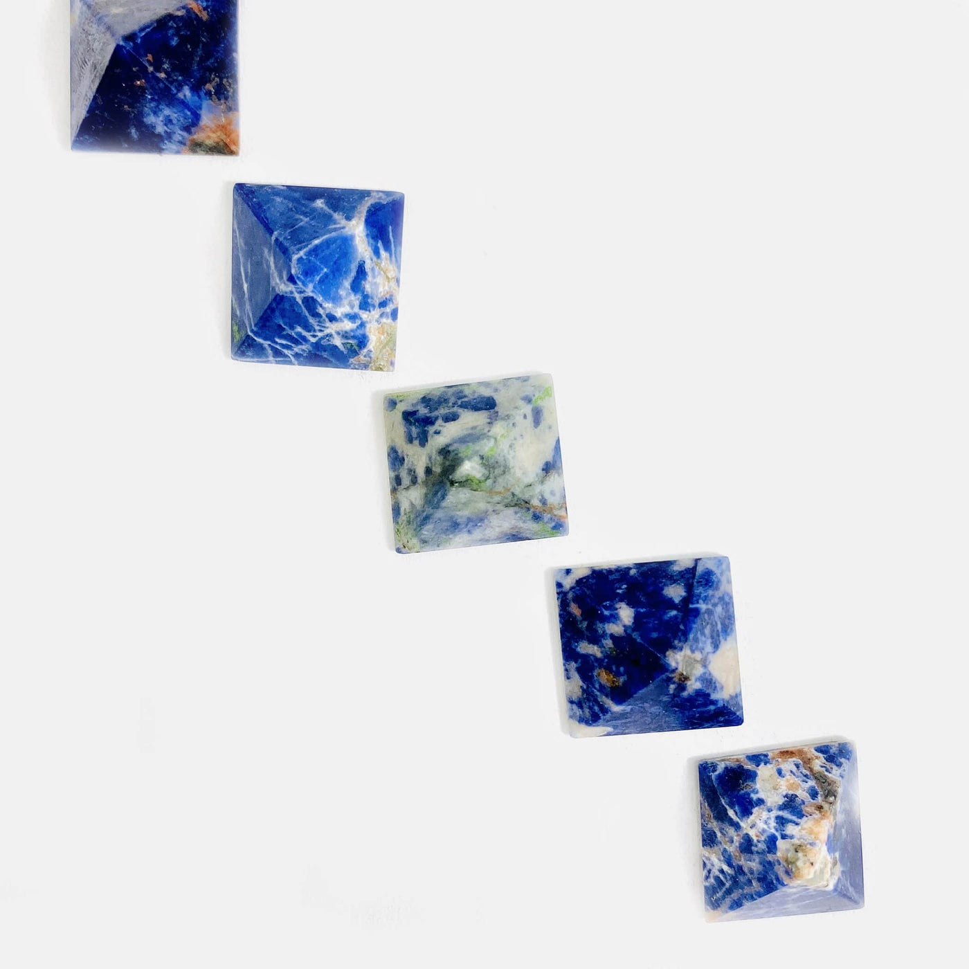 overhead view of five sodalite small pyramids in a diagonal line on white background