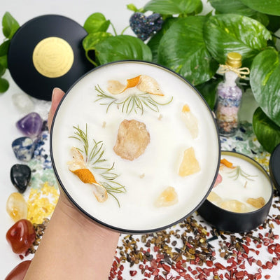 hand holding up Solar Plexus Chakra Candle Tin with decorations in the background
