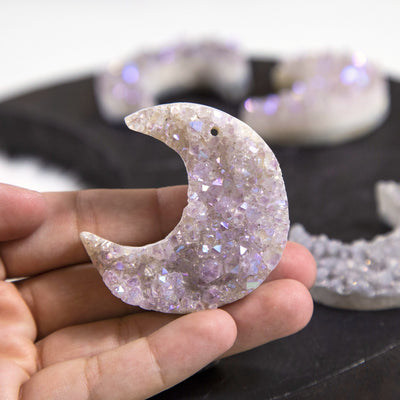hand holding up moon shaped titanium druzy pendant for size reference with others blurred in the background