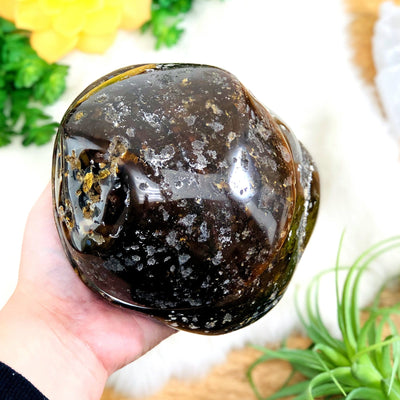 Top view of polished agate druzy box closed in a hand displaying the external surface. Plants in the background.