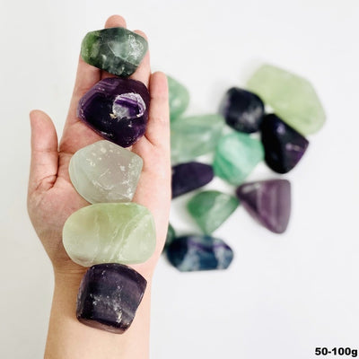 Hand holding up 5 Rainbow Fluorite Tumbled Stones over pile of stones blurred on white background