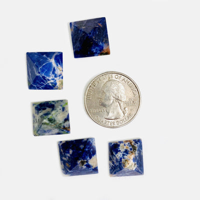 overhead view of five sodalite small pyramids surroundin a quarter on white background for size reference