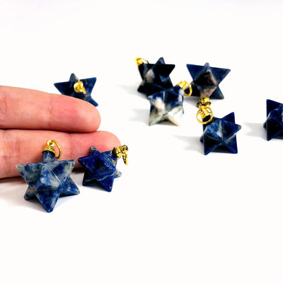 many sodalite merkaba stars on white background with two in front of fingers for size reference