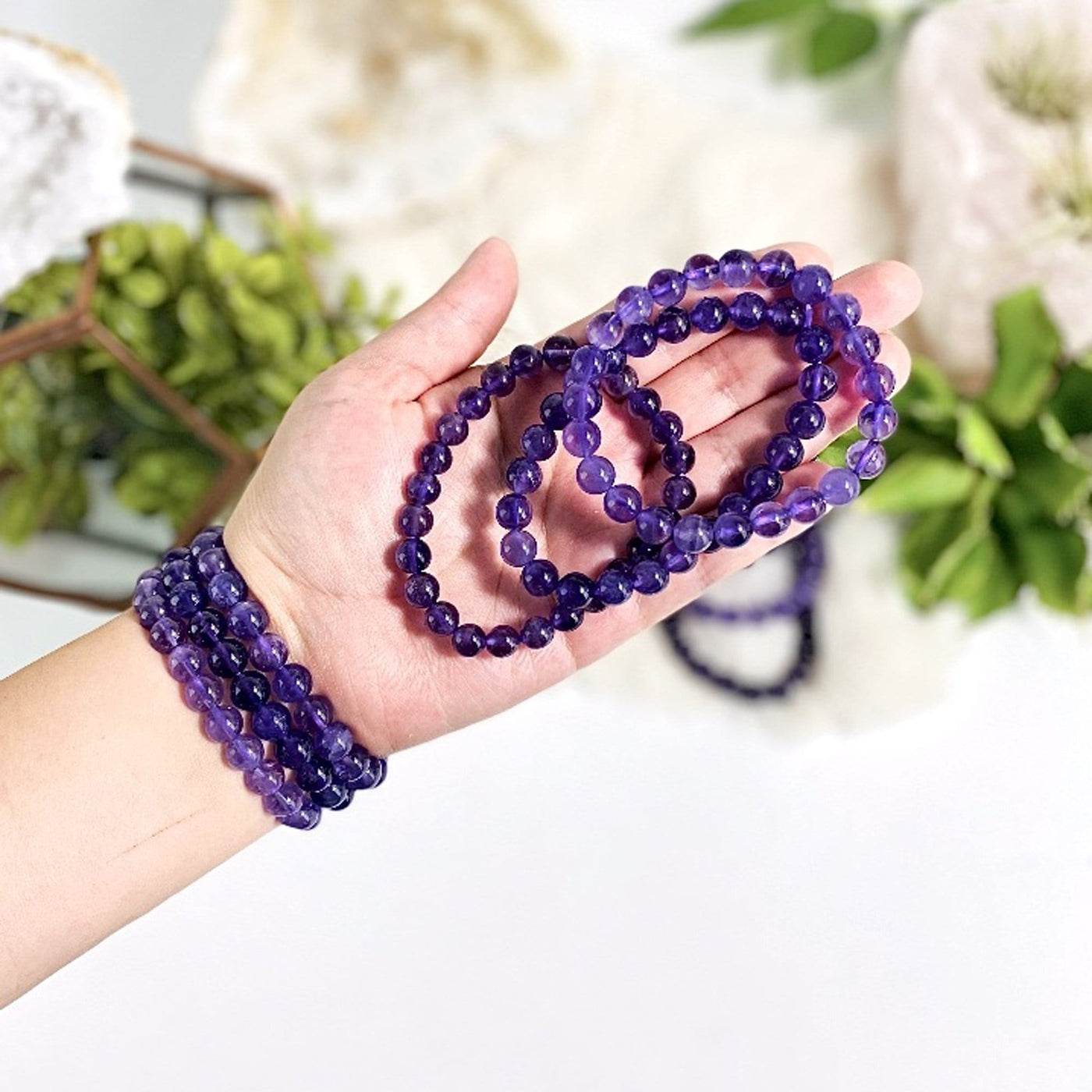 Amethyst gemstone bracelets.  Three are on a woman's wrist and three are held in her hand.
