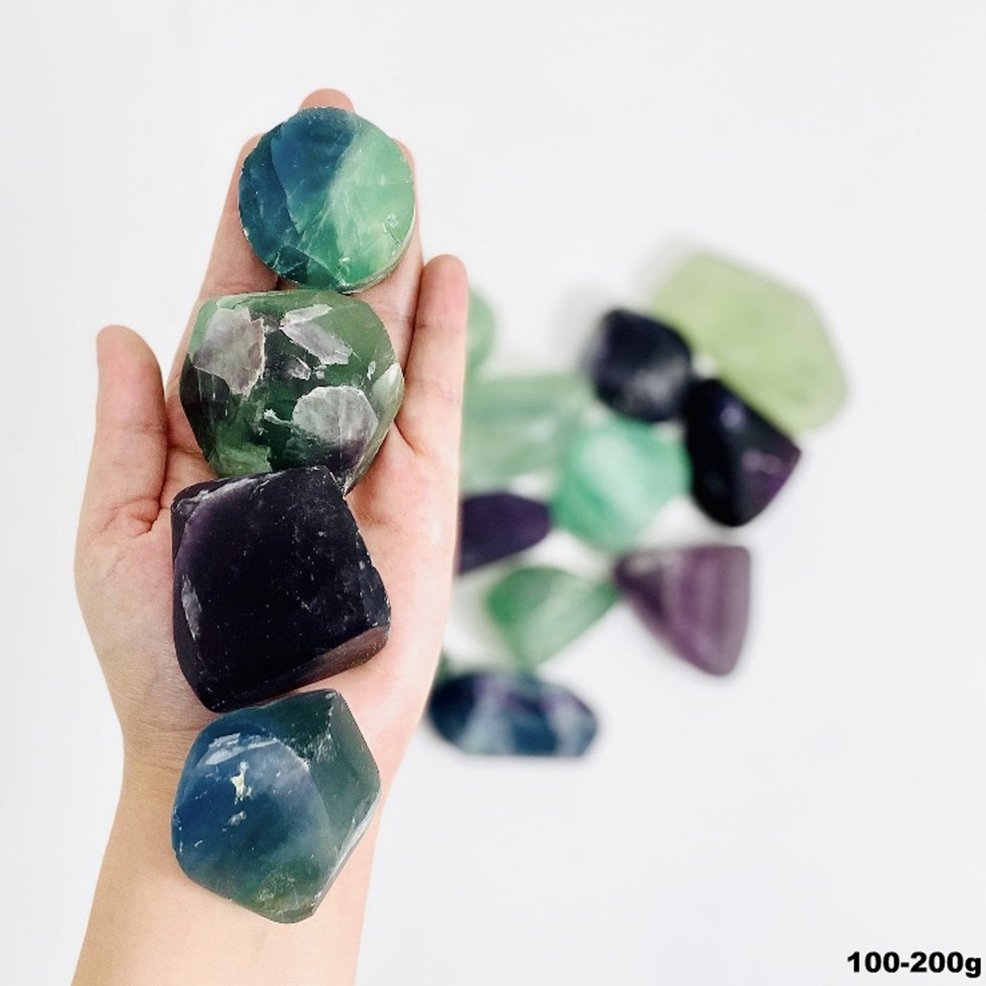 Hand holding up 4 Rainbow Fluorite Tumbled Stones over pile of stones blurred over white background