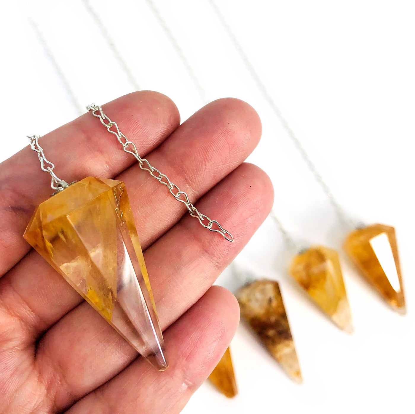 hand holding up golden healer quartz pendulum with others in the background
