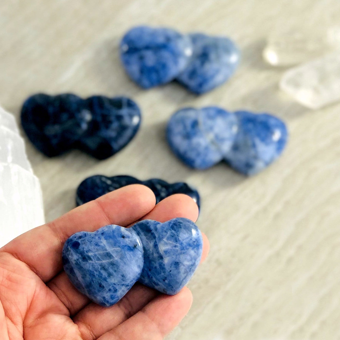 one sodalite double heart shaped stone in hand for size reference with four others in background