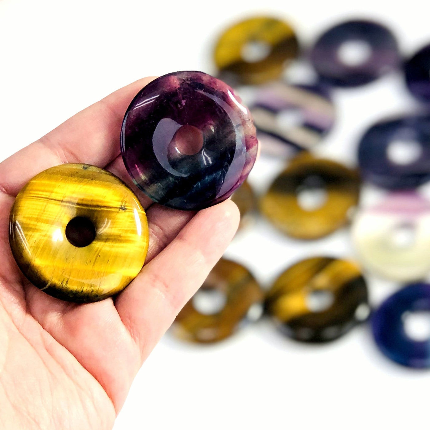 hand holding up 2 donut shaped polished stones with others blurred in the background