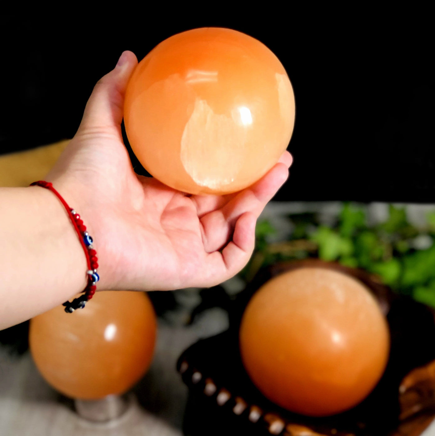 hand holding up Orange Selenite Sphere with decorations in the background