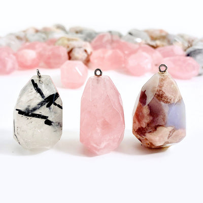 1 of each Rose Quartz Rutilated Quartz Flower Agate Pendants in focus with others blurred on white background