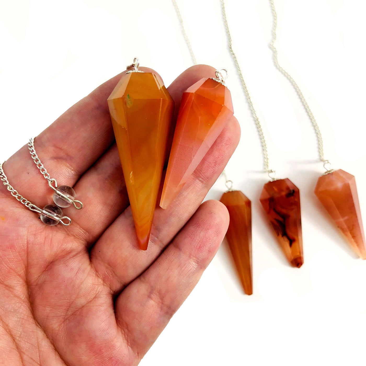 2 carnelian pendulums in hand with 3 others in the background with a white backdrop
