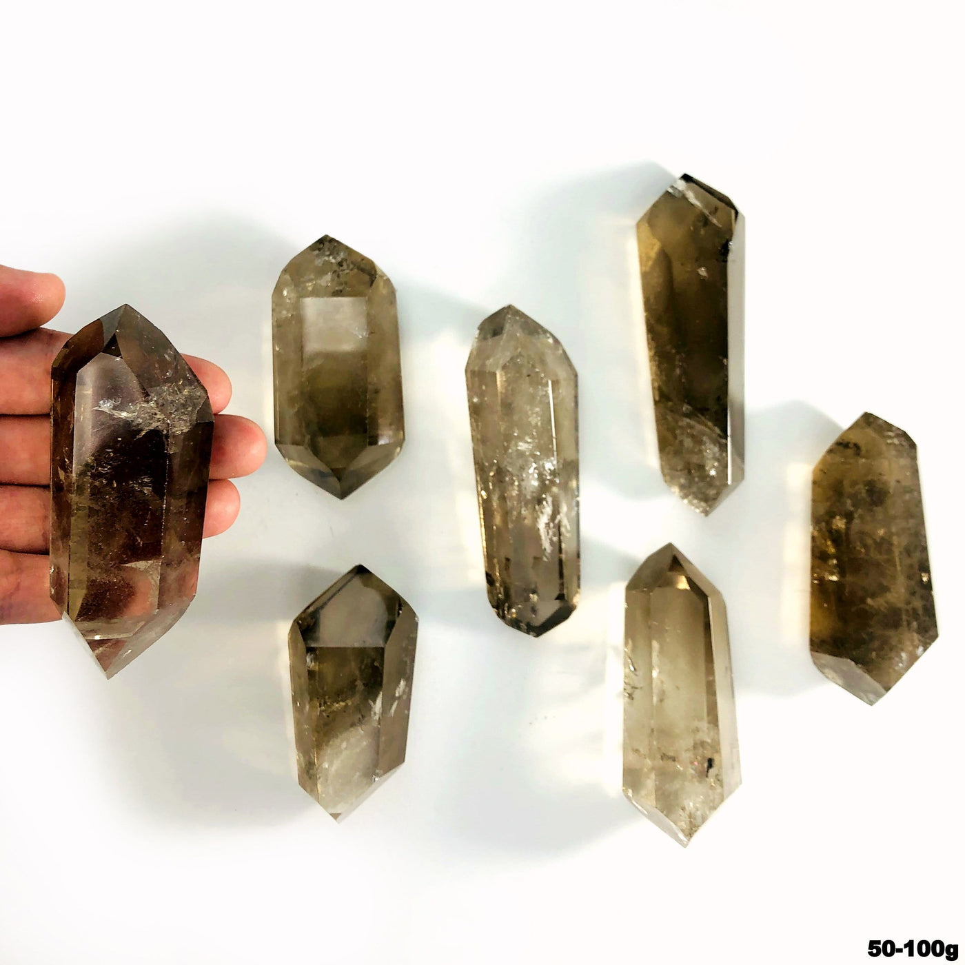 overhead view of many 50g - 100g smokey quartz double points on white backdrop with one in hand for size reference
