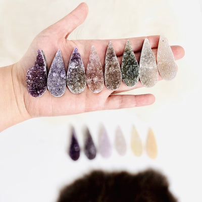 hand holding up 8 druzy teardrop cabochons with decorations blurred in the background
