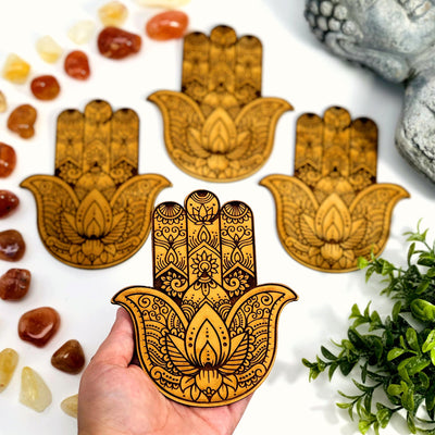 one hamsa hand wooden alter display pictured on a hand above others for size reference