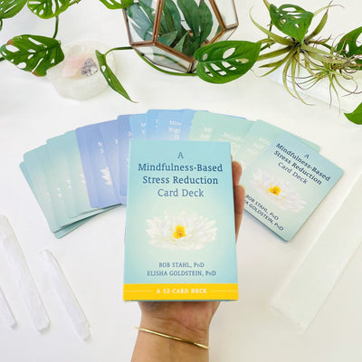 A Mindfulness-Based Stress Reduction Card Deck in a hand and card deck expanded in the background.