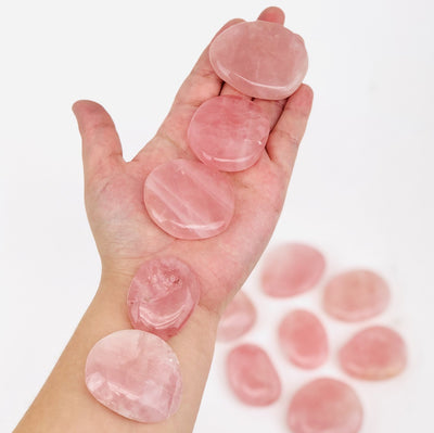 Hand holding up 5 Rose Quartz Palm Stones with other blurred on white background