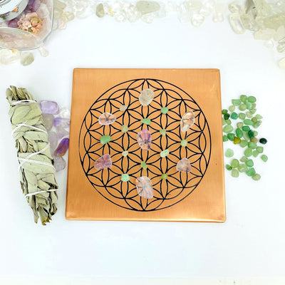 copper square flat plate with a flower of life grid in black on it displayed with assorted crystals on the grid