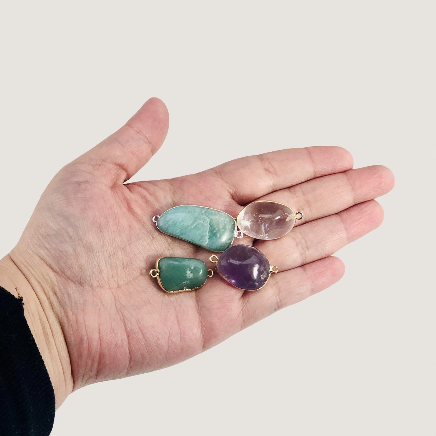 hand holding up 4 gemstone connector pendants on white background