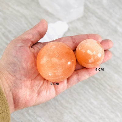 orange selenite spheres in hand to show 5m and 4cm size reference