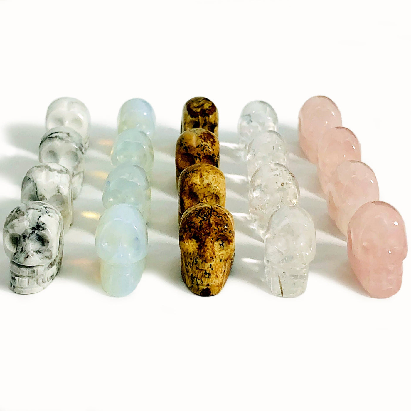 white howlite, opalite, picture jasper, crystal quartz, and rose quartz skull beads in rows on white background