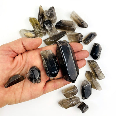 Polished Smoky Quartz Tumbled Stones and Points on a table and some in a hand to show varying sizes