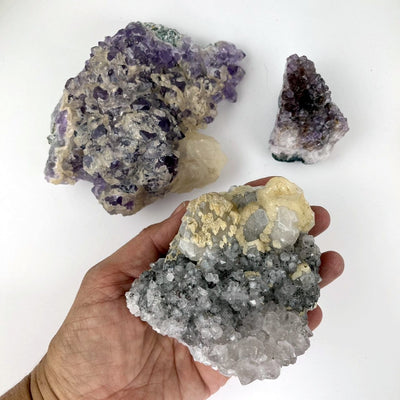 3 pieces of Amethyst, one in a hand for size reference