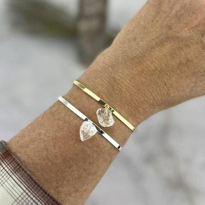 Gold and silver bracelet on a woman's wrist.  Both have a rough crystal quartz stone dangling from the center of the bracelet.