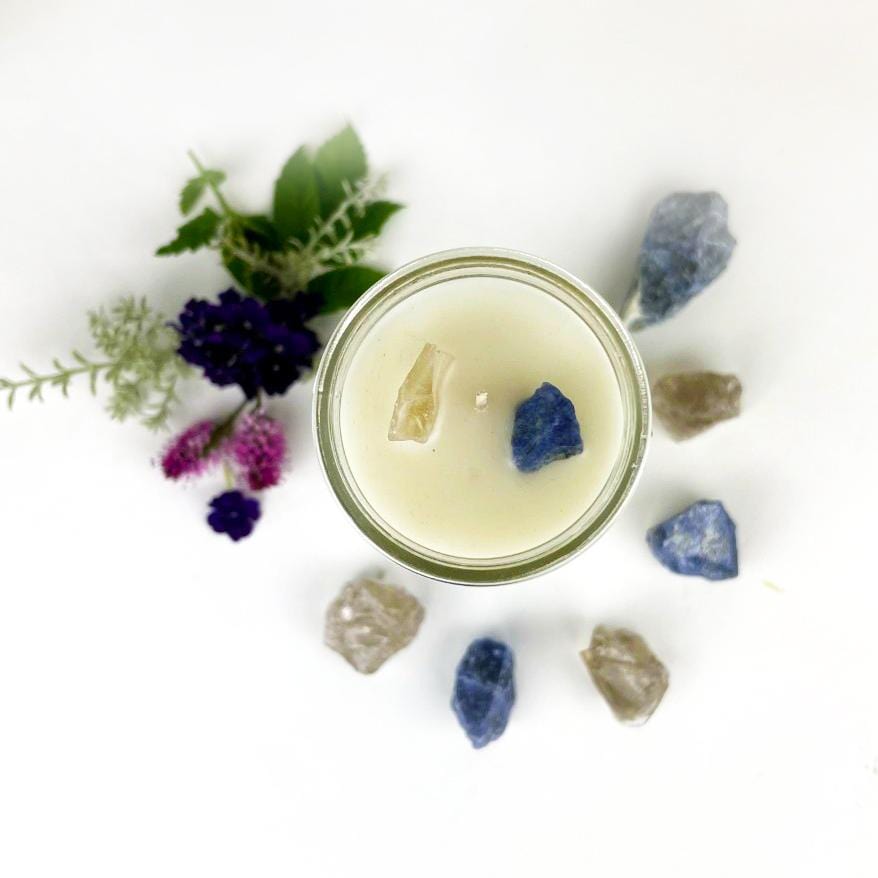 Top view of Release Intention Candle surrounded by crystals and flowers on white background