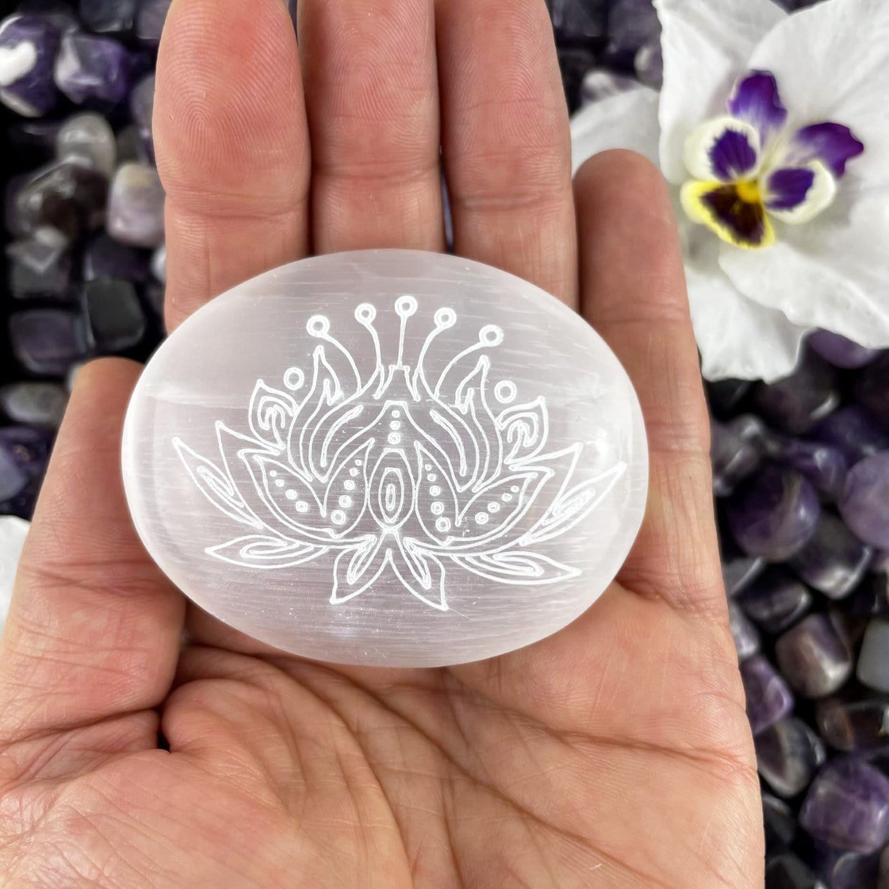 close up of one selenite lotus engraved palm stone in hand for size reference and details