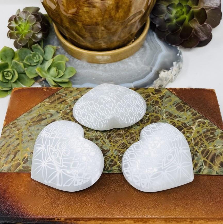 close up of three selenite stone hearts with eye engraving on display for possible variations
