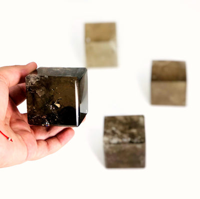 close up of one smokey quartz cube in hand for size reference with three others in white background