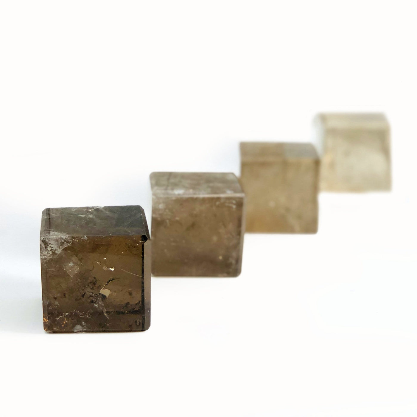 four smokey quartz cubes in a diagonal line on white background with the first one in focus for possible variations