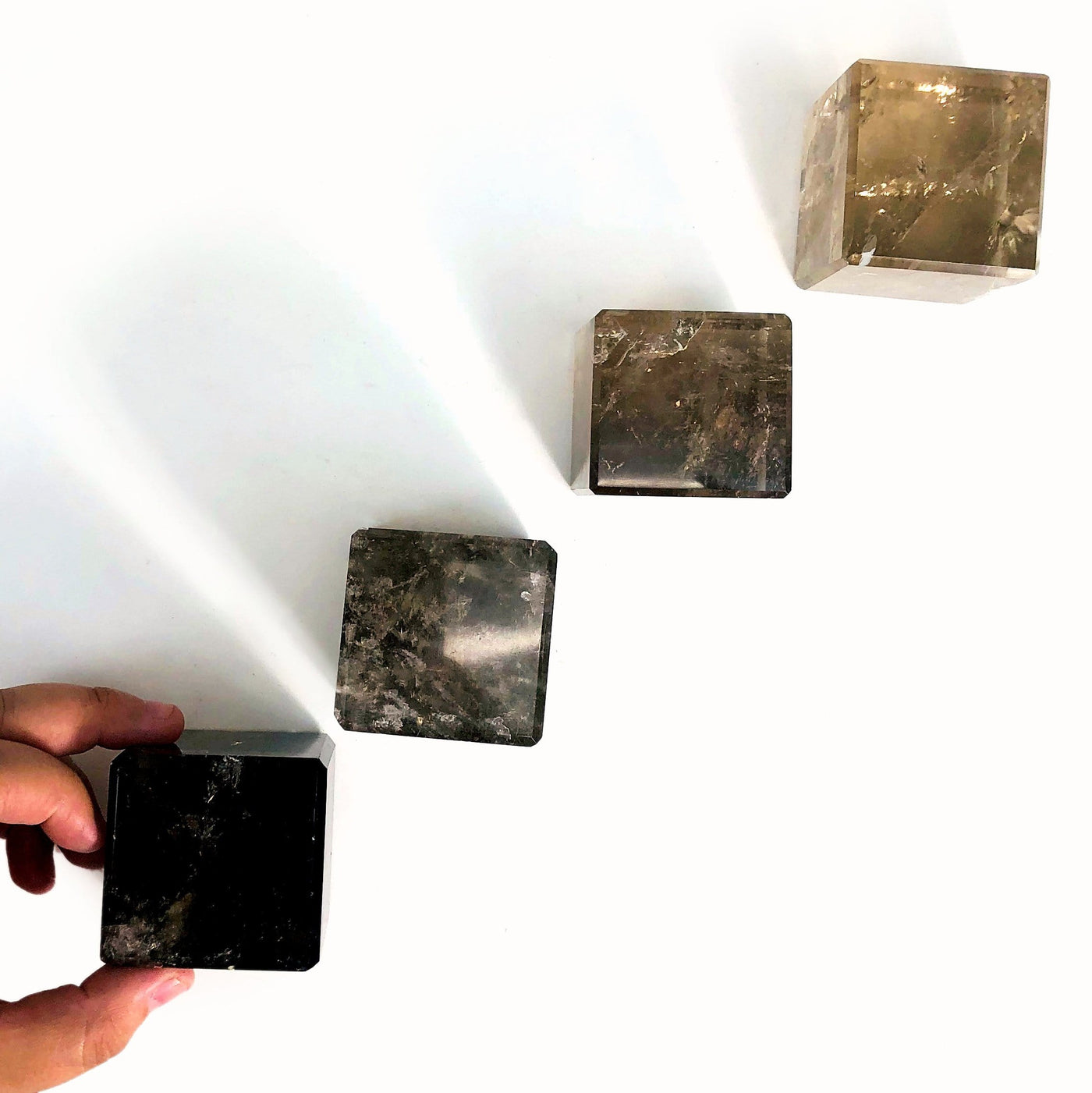 overhead view of four smokey quartz cubes in a diagonal line with the first on in hand for size reference