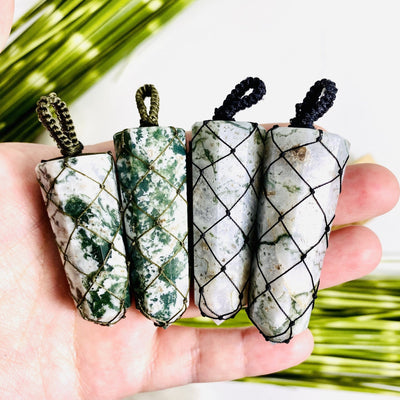 hand holding up 4 moss agate netted pendants with decorations in the background